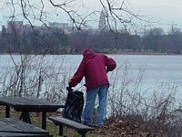 During a winter cleanup, a volunteer puts debris in a plastic bag, the skyline of Alexandria, VA is in the background.