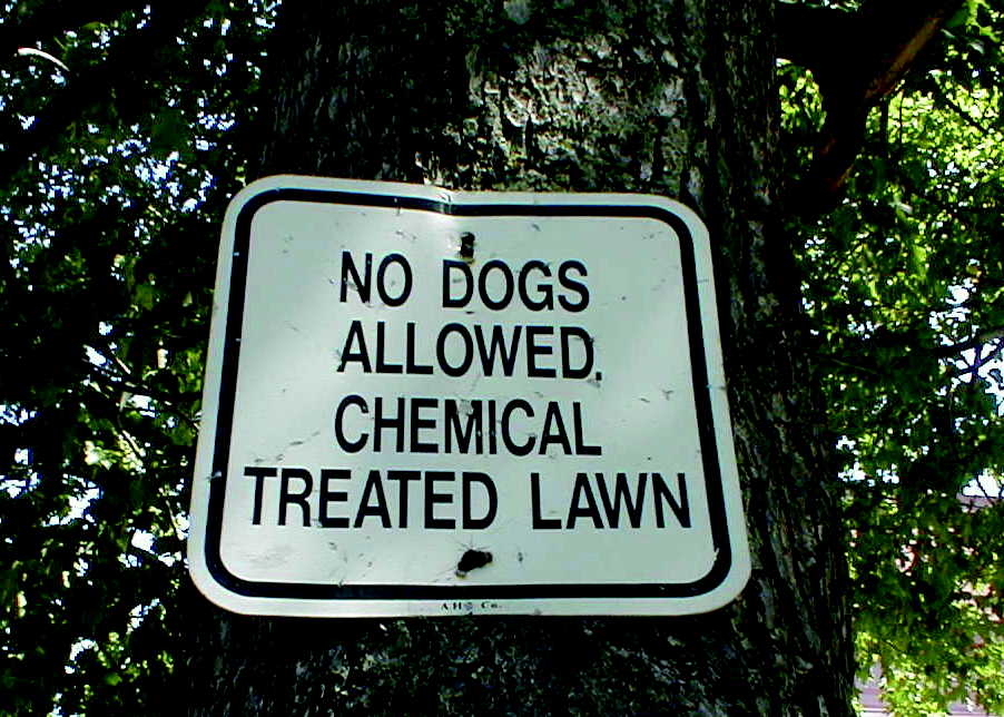 Warning sign on a tree notifying the community to keep pets off the lawn recently treated with pesticides.