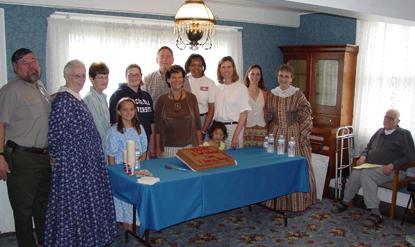 Image of staff and volunteers standing around a cake commemorating the McLoughlin House Site's third anniversary