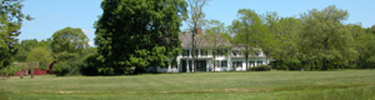 William Floyd Estate manor house and outbuildings among trees in full summer foliage.