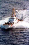A Coast Guard patrol boat travelling at high speed, with large numbers of people on deck.