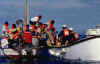 A picture of a Coast Guard small boat alongside a small sail boat, offloading Haitian migrants.