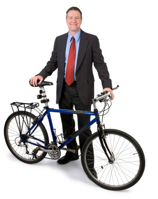 Photograph of a man in a business suit standing next to a bicycle.