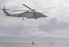 Image of helicopter with responder hovering over water rescuing a victim. Click for larger image.