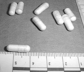 Photograph of 2C-B capsules with a ruler at the bottom of the photo. One capsule laid alongside the ruler for comparison measures one and one-half centimeters in length.
