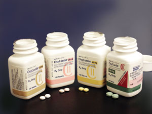 Photo of four uncapped OxyContin bottles with two pills displayed in front of each bottle.