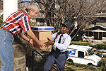 Image 4: A letter carrier accepting packages from a residential customer on the front porch of their home.