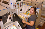 Image 9: A smiling female plant worker monitors flat packages being sorted on the Automatic Sorting Machine (ASM).