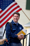 Image 5: A smiling letter carrier on his route with an American flag in the background.