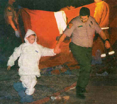 Photo of a small boy wearing a protective suit being led by a man in California Department of Forestry uniform.