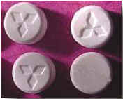 Photograph of 4 round, white pills stamped with three diamond shapes forming a triangle.