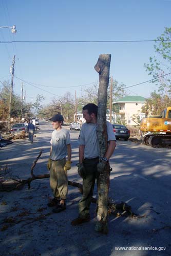 Two AmeriCorps members look on as teammates cut and clear fallen trees and other debris from Second Street in Pass Christian, Miss.
