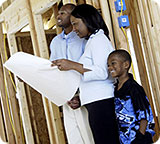 A man, woman and little boy standing inside their new house while it is being constructed; the woman is looking over the plans.