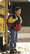 A boy standing outside a school bus door.