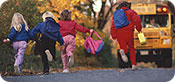 Three girls and one boy running towards a school bus.
