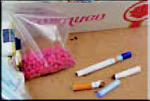 Photograph showing comparison of  small pink tablets in a baggy beside a pen and cigarette.