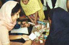 Photo of woman sitting at a table and reading information about medicine on a table.