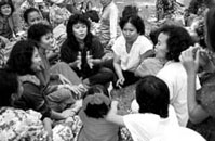 Photo of several Asian women smiling and sitting in a circle, meeting.