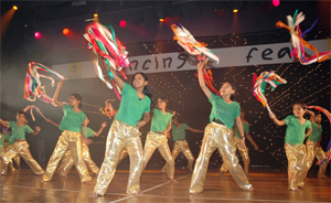 Children dance with ribbons in a gymnasium before an audience.