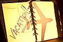 A planner with the word 'vacation' across the page; and a shadow of an airplane.