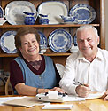 An older man and woman sitting at a dining room table doing paperwork.