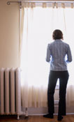 A woman standing next to a radiator heater; linking to Low Income Home Energy Assistance Program