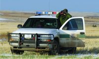 Officer looking through binoculars with resting on SUV