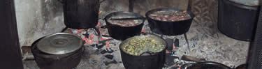 Pots of stew, potatoes, wild rice and vegetables simmer over hot coals in the kitchen's fireplace.