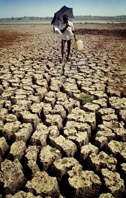 Celebrate Earth Day. It's good for the planet, and good for your health. Photo of A man shades himself from the sun with an umbrella as he carries drinking water across the dry bed of a river.