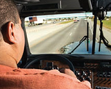 Image of an eighteen wheeler cab, its driver, and the road ahead