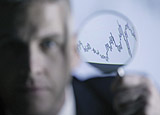 Man with magnifying glass viewing line graph