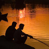 photo of two people fishing in the light of an orange sunset