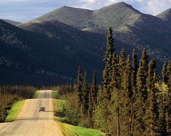 Car drives down the Dalton Highway with Brooks Range mountains in the background