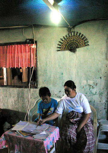 In their newly electrified home in Tawi-Tawi, in the southern Philippines, Mrs. Arik helps her son do his homework at night with the help for fluorescent lighting.