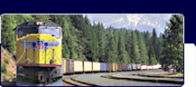 Train passing pines with mountain peaks in the
background.