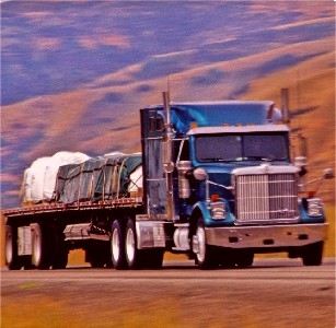 Cover Photo: Flatbed combination truck with blue cab on highway.
