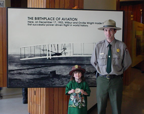 Park ranger and Junior Ranger standing in front of First Flight photograph.