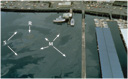 Aerial view of oil spreading out into metallic or dull brown layer, rainbow and silver/gray sheens in and around piers.