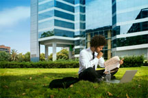 Man sitting on a lawn in front of building with laptop