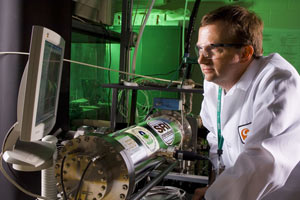 Image: Scientist wearing goggles and lab coat monitoring a computer read-out.