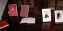 Three hard-bound books and portraits from the late 1800s are lined up on a dark table.