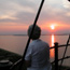 Silhouetted woman watches colorful sunset from atop the lighthouse.