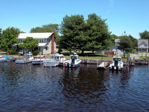 Park boats moored at dock in front of building along the river, park sign in front of shaded lawn.