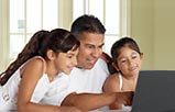 Un padre latino sentado con una hija a cada lado usando una computadora.
