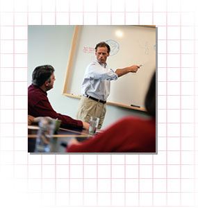 A man writing on a whiteboard in a meeting.