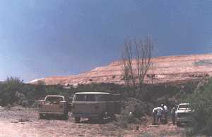 USGS scientists conducting field work at a well site with a view of a large tailings pile in the background