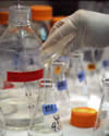 glass beakers and bottles. A hand is pouring a liquid into the foremost beaker.