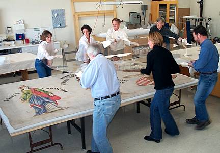 Conservators place an acrylic glazing panel over a large painted banner from Fort Pulaski NM