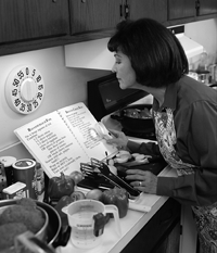 Una mujer usa una lupa para leer el libro de recetas en su cocina.