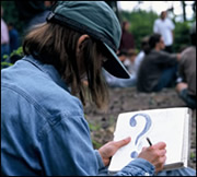 [Photograph]: Student taking notes at an outdoor lecture.